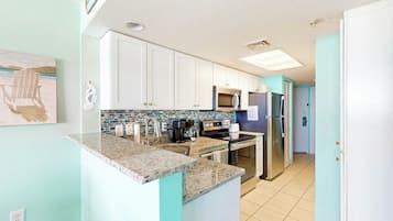 A kitchen with white cabinets, a granite countertop, a microwave, a refrigerator, and a tiled backsplash.