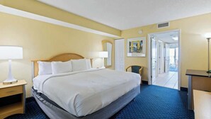 A hotel room with a bed, a desk, a chair, and a door leading to another room. - Bay Watch Resort 1603 (North Myrtle Beach)
