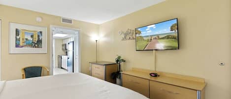 Habitación de hotel con una cama grande, un escritorio con cajones, un televisor montado en la pared y una puerta que da al baño.