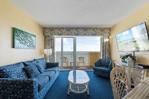 Ein Zimmer mit einer Couch, Stühlen, einem Tisch, einem Fernseher und einem Balkon mit Blick.