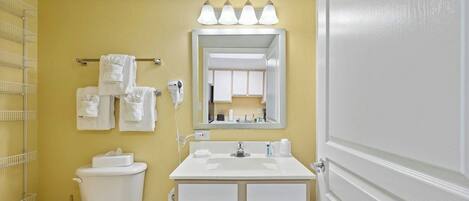 A bathroom with a toilet, sink, and mirror. There are towels hanging on a rack, and a shower area is visible.