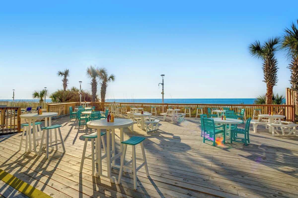 Una terraza al aire libre con mesas y sillas, con vista a un cuerpo de agua.