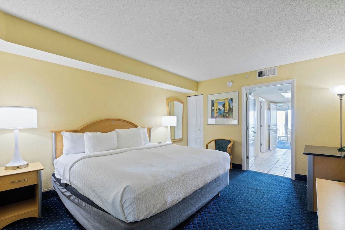 Une chambre d’hôtel avec un lit, des tables de chevet, un bureau et une chaise. Une porte donne accès à un balcon.