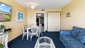 A room with a dining table and chairs, a sofa, a ceiling fan, and a door leading to another room. - Bay Watch Resort 1603 (North Myrtle Beach)