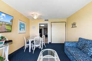 A room with a dining table and chairs, a sofa, a ceiling fan, and a door leading to another room. - Bay Watch Resort 1603 (North Myrtle Beach)