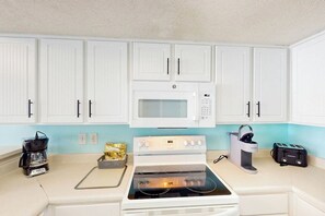 A kitchen with white cabinets, a microwave, a stove, a coffee maker, and a toaster. - Bay Watch Resort 1605 (North Myrtle Beach)