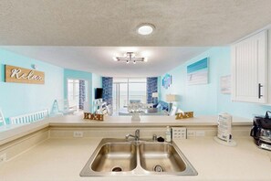 A kitchen with a double sink, a countertop, and a dining area with a table and chairs. - Bay Watch Resort 1605 (North Myrtle Beach)