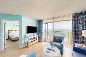 Una habitación de hotel con balcón, una cama, televisor, una mesita de centro y zona de estar.