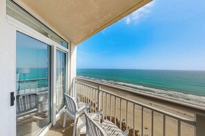 A balcony with a view of the ocean, a glass door, and two white chairs. - Bay Watch Resort 1605 Oceanfront (North Myrtle Beach)