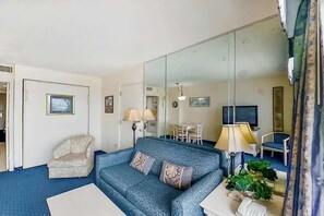 Ein Wohnzimmer mit Sofa, Sessel, Lampe, Telefon und Spiegel.