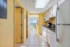 A kitchen with a view to the outside, a door leading to a balcony, and a refrigerator. - Bay Watch Resort 1503 (North Myrtle Beach)