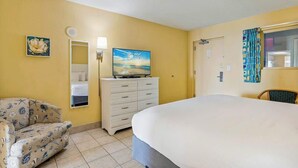 Ein Hotelzimmer mit einem Bett, einem Schreibtisch, einem Sessel, einem Fernseher und einem Gemälde an der Wand.