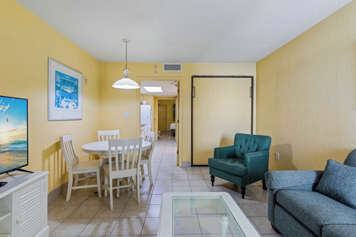 A living room with a television, a dining table with chairs, a sofa, and a glass coffee table.