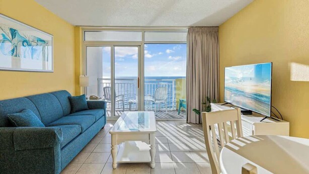 Ein Zimmer mit einer Couch, einem Glastisch, einem Fernseher und einem Balkon mit Blick.