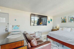 Ein Hotelzimmer mit einem Bett, einer braunen Ledersofa, einem kleinen Beistelltisch, einer Wanduhr und Kunstwerken.