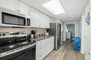 A modern kitchen with white cabinets, a stainless steel refrigerator, a microwave, and a stove. - Bay Watch Resort 1506 (North Myrtle Beach)