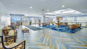 A spacious lobby with a herringbone patterned floor, seating areas with wicker furniture, and a view of the sea through large windows. - Bay Watch Resort 1506 (North Myrtle Beach)