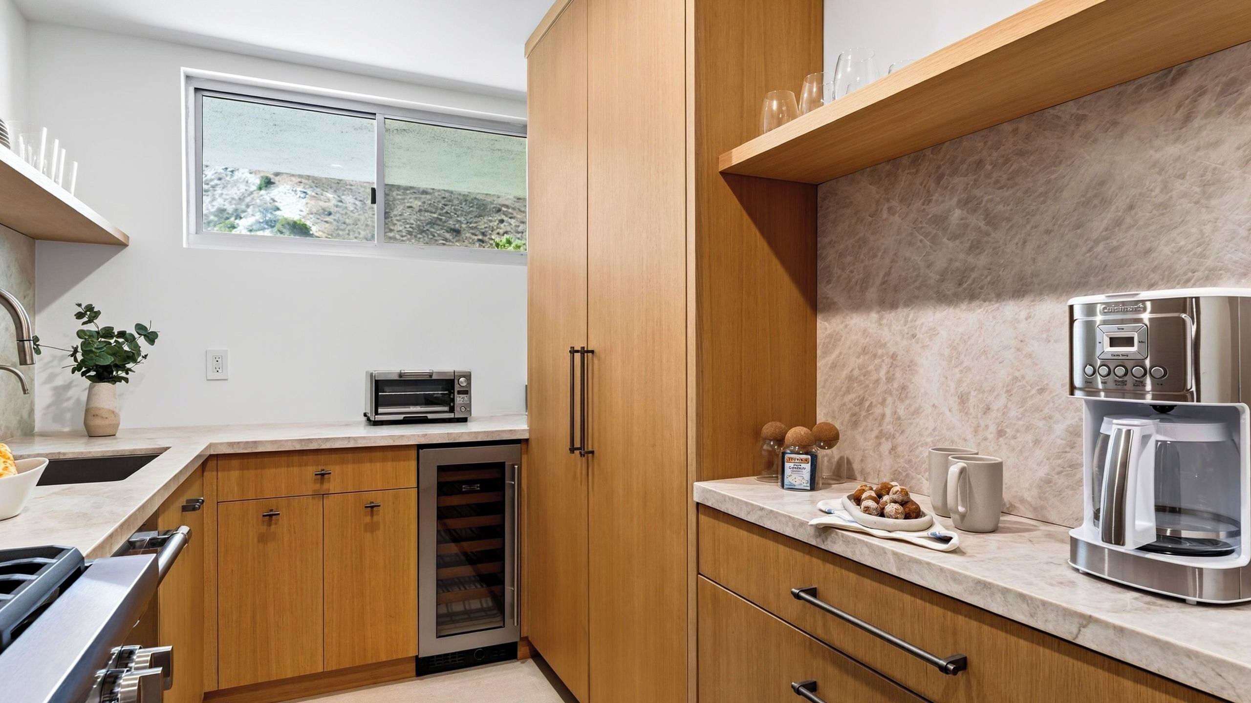 Une cuisine moderne avec des meubles en bois, un four encastré, une machine à café et une fenêtre donnant sur l’extérieur.