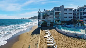 A beachfront hotel with a pool, beach chairs, and a view of the ocean.