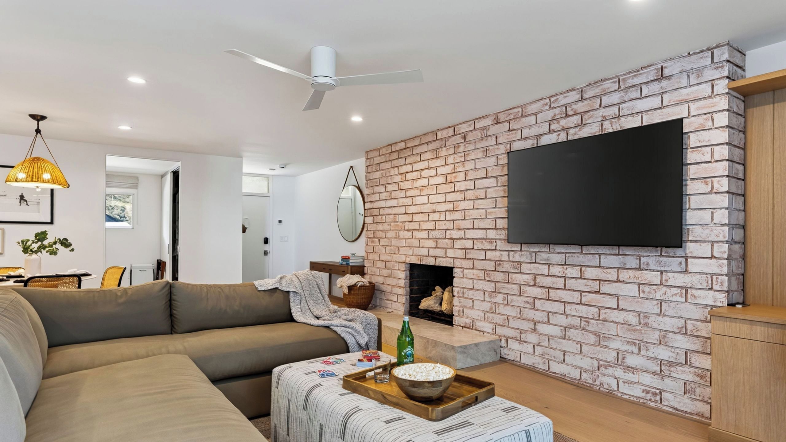 Een moderne woonkamer met een bakstenen muur, een flatscreen televisie, een plafondventilator en een bank.
