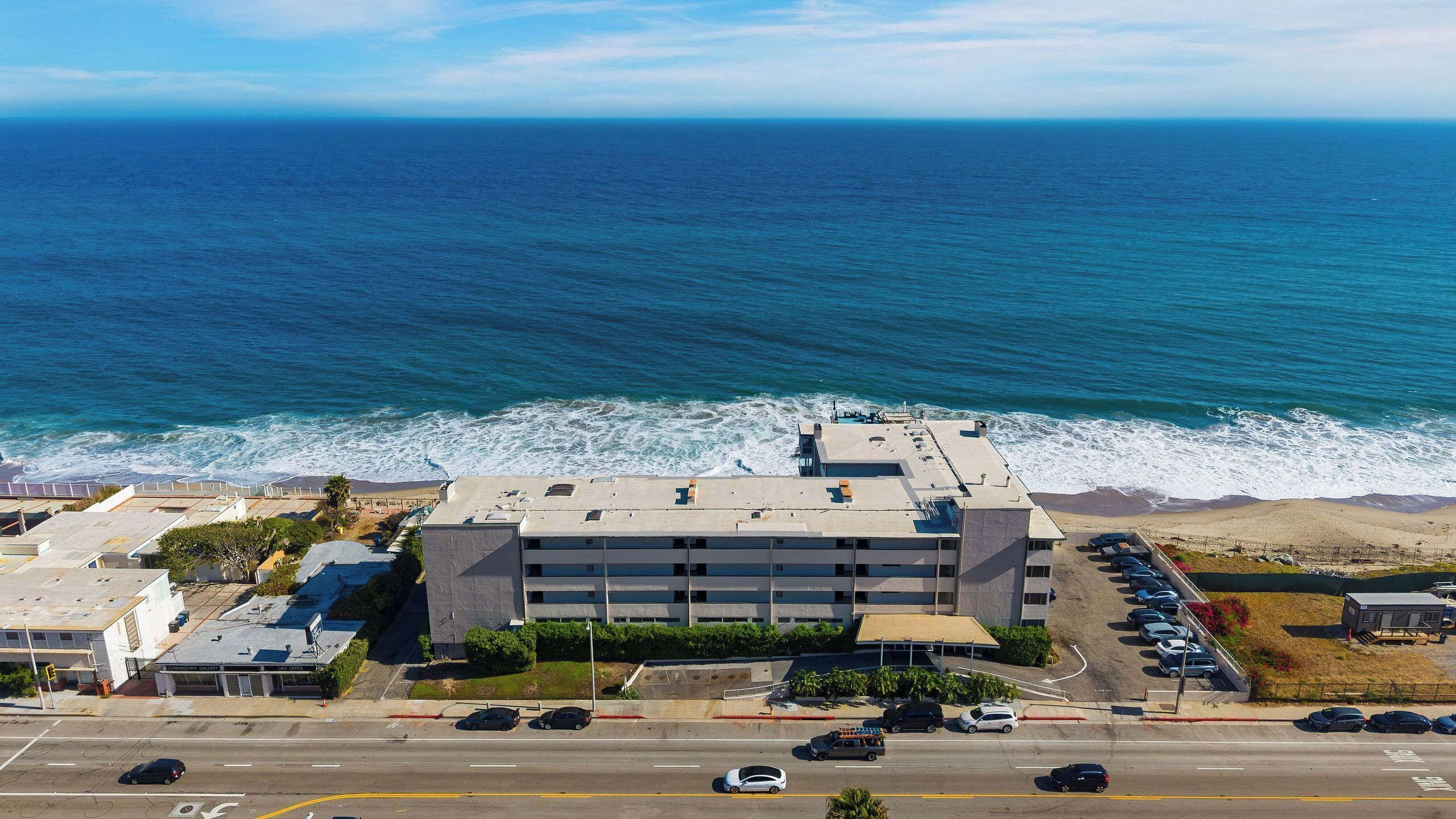 Un edificio de varios pisos con un estacionamiento frente a él, con vista a una playa y al océano.