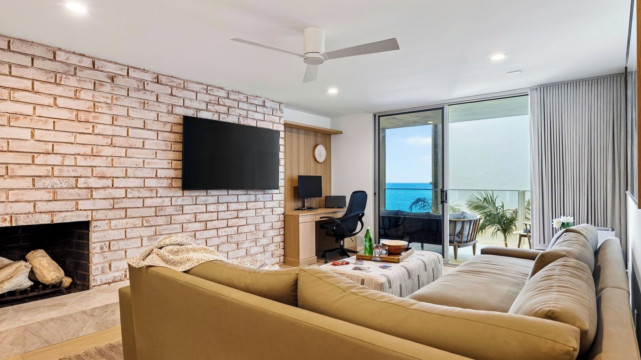 Un salon avec un mur en briques, un téléviseur à écran plat, une cheminée, un canapé, un coin repas avec une table et des chaises, et un balcon avec vue.