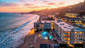 A beachfront hotel with a pool, beach chairs, and a view of the ocean.