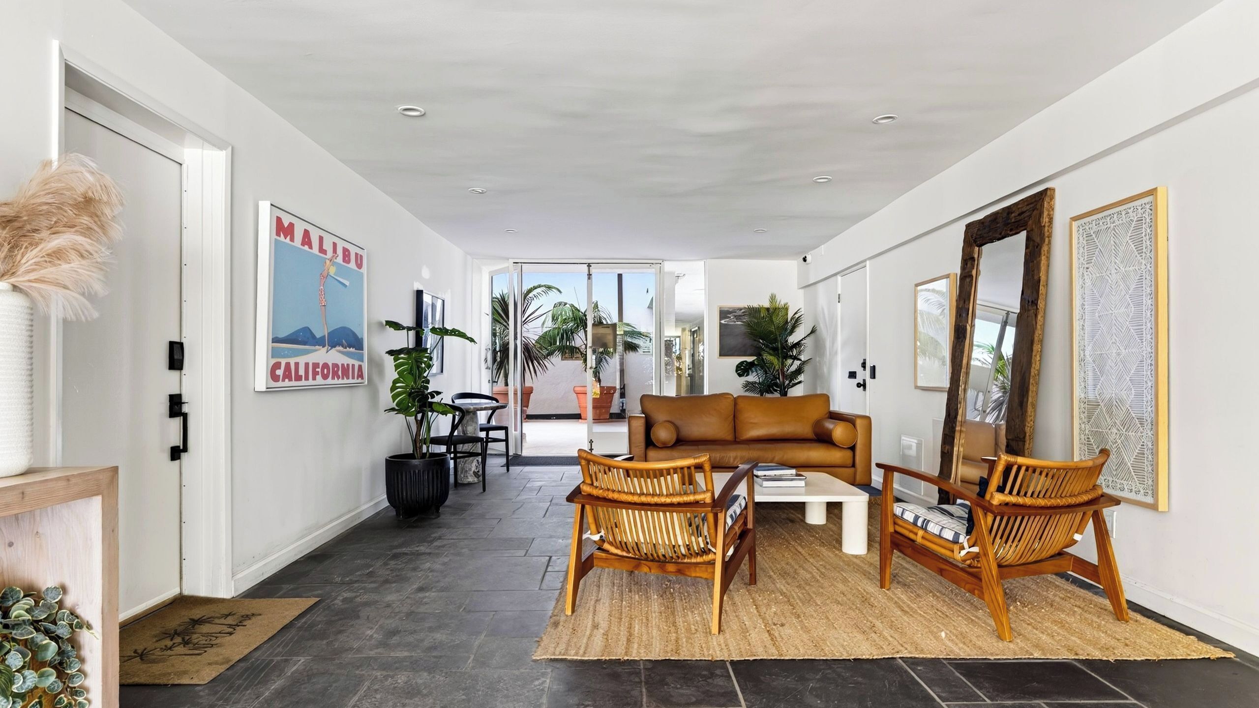 Een moderne woonkamer met een bank, twee rotan stoelen, een salontafel en een grote spiegel.