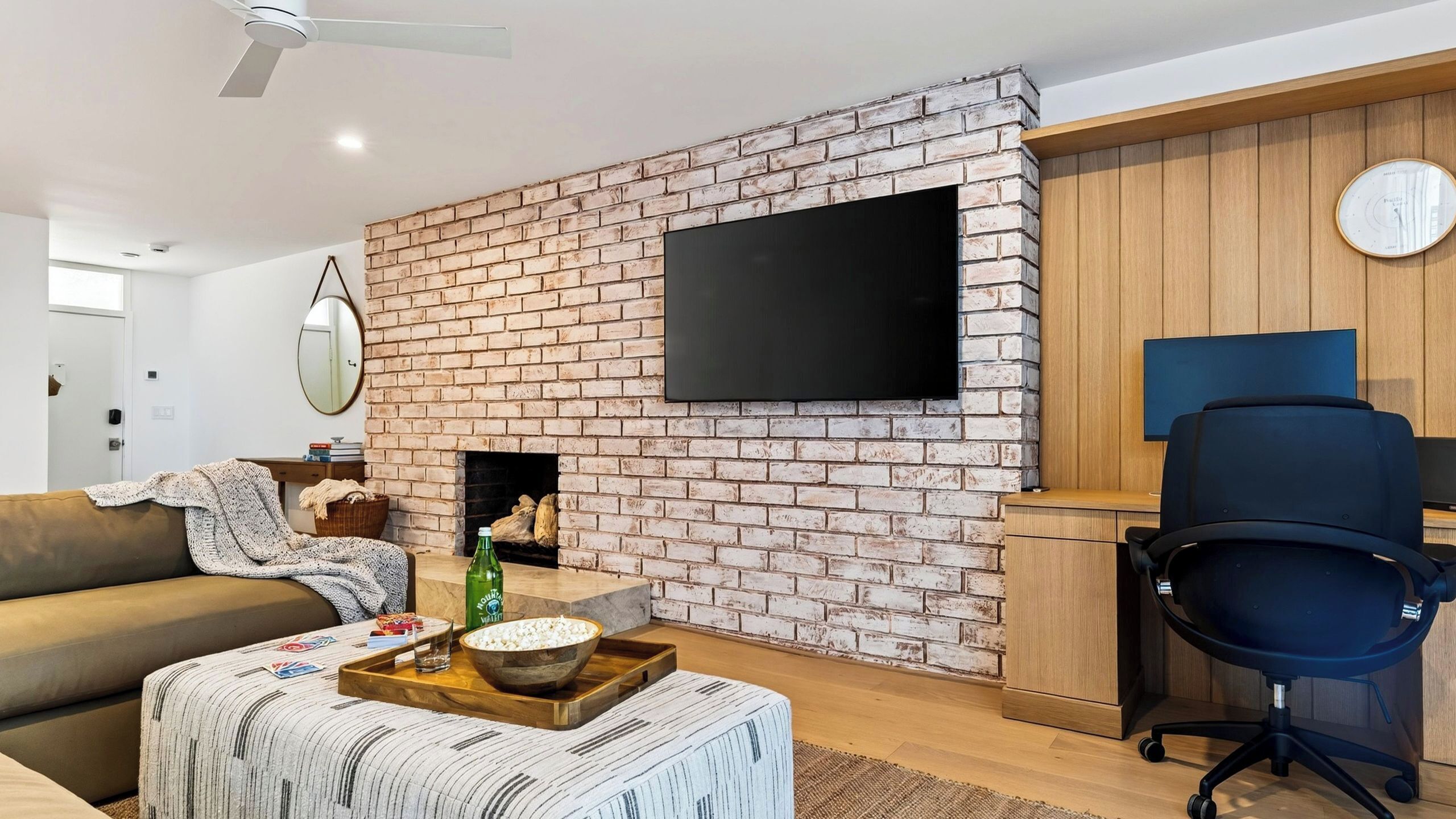 Een woonkamer met een bakstenen muur, een flatscreen televisie, een bank, een salontafel met lekkernijen en een houten kast.