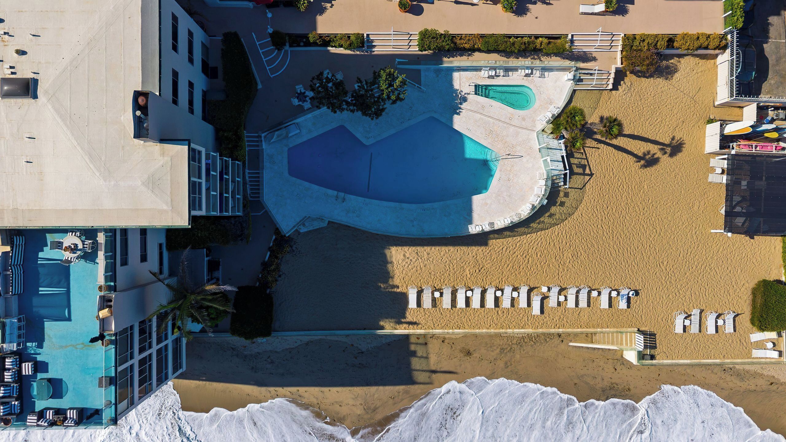 Vue aérienne d’un complexe hôtelier doté d’une grande piscine, de plusieurs espaces de détente et d’une plage de sable.