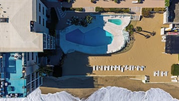 En vy från ovan av ett semesterområde med en stor pool, flera avslappningsområden och en sandstrand.