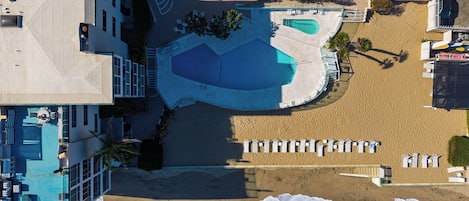 Vue aérienne d’un complexe hôtelier doté d’une grande piscine, de plusieurs espaces de détente et d’une plage de sable.