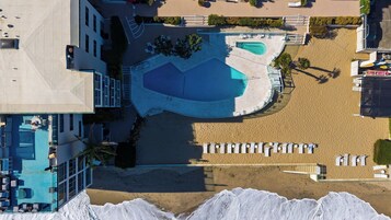 An aerial view of a resort with a large pool, multiple lounge areas, and a sandy beach.