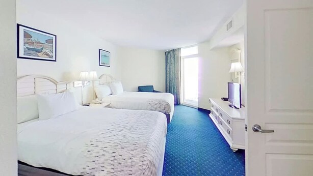 A hotel room with two beds, a dresser, a television, and a window with curtains. - Bay Watch Resort 1512 (North Myrtle Beach)