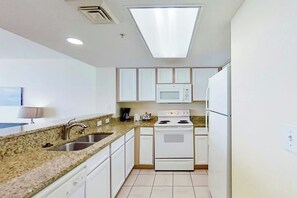 A kitchen with white cabinets, a microwave, a stove, and a sink. - Bay Watch Resort 1512 (North Myrtle Beach)