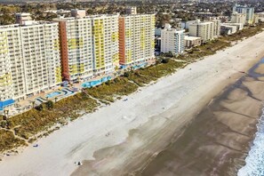 A beachfront hotel with multiple high-rise buildings, a sandy beach, and a swimming pool area. - Bay Watch Resort 1512 (North Myrtle Beach)