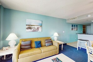 Uma sala de estar com sofá, duas mesas laterais com luminárias, uma mesa de centro e um quadro na parede.