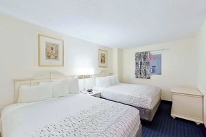 Ein Hotelzimmer mit zwei Betten, einem Nachttisch, einer kleinen Kommode und einem Fenster mit Vorhängen.