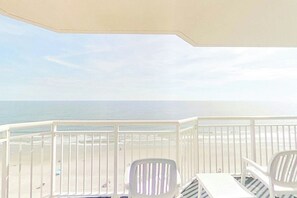 A balcony with a view of the beach and ocean, white chairs, and a table. - Bay Watch Resort 1611 (North Myrtle Beach)