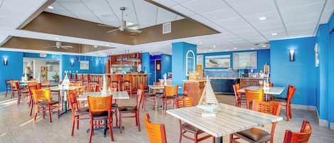 Un restaurante amplio con varias mesas y sillas, una zona de cocina y una pared de acento azul.