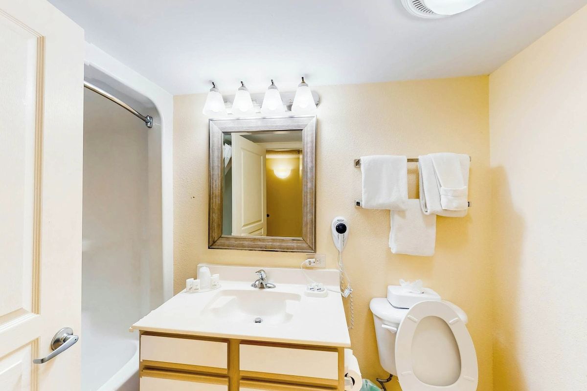 Ein Badezimmer mit Waschbecken, Toilette und Dusche. Handtücher hängen an der Wand und über dem Waschbecken hängt ein Spiegel.
