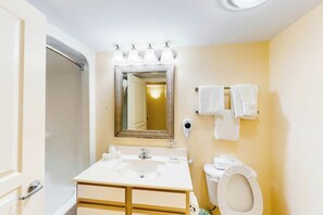 Un baño con lavamanos, inodoro e ducha. Hay toallas colgadas en la pared y un espejo sobre el lavamanos.
