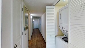 A laundry room with a washing machine and dryer, a wooden floor, and a hallway leading to other rooms. - Bay Watch Resort 1612 (North Myrtle Beach)