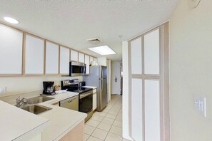 A modern kitchen with stainless steel appliances, a microwave, and a coffee maker. - Bay Watch Resort 1613 (North Myrtle Beach)