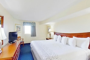 A hotel room with a bed, a desk with a television, a chair, a lamp, and a window with curtains. - Bay Watch Resort 1613 (North Myrtle Beach)