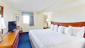 A hotel room with a bed, a desk with a television, a chair, a lamp, and framed pictures on the walls. - Bay Watch Resort 1613 (North Myrtle Beach)