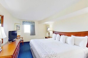 A hotel room with a bed, a desk with a television, a chair, a lamp, and framed pictures on the walls. - Bay Watch Resort 1613 (North Myrtle Beach)
