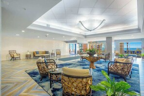 A spacious lobby with wicker furniture, a central coffee table, and a view of the sea through large windows. - Bay Watch Resort 1617 (North Myrtle Beach)