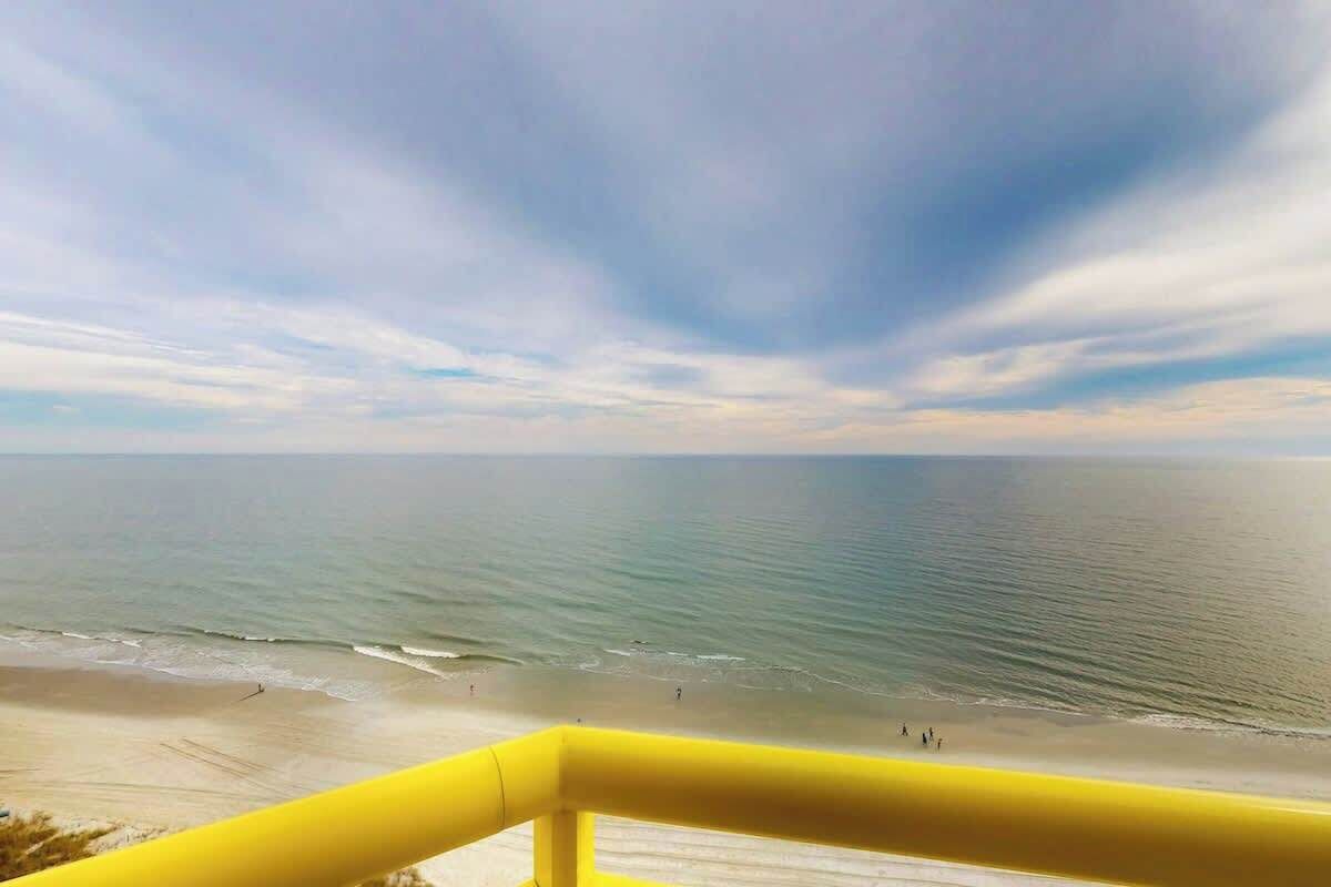 Blick auf einen Strand mit gelister Stützmauer, ruhiger See und blauem Himmel.
