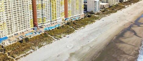 Un hôtel situé en bord de mer, composé de plusieurs immeubles de grande hauteur, doté d’une plage de sable et d’un espace piscine.